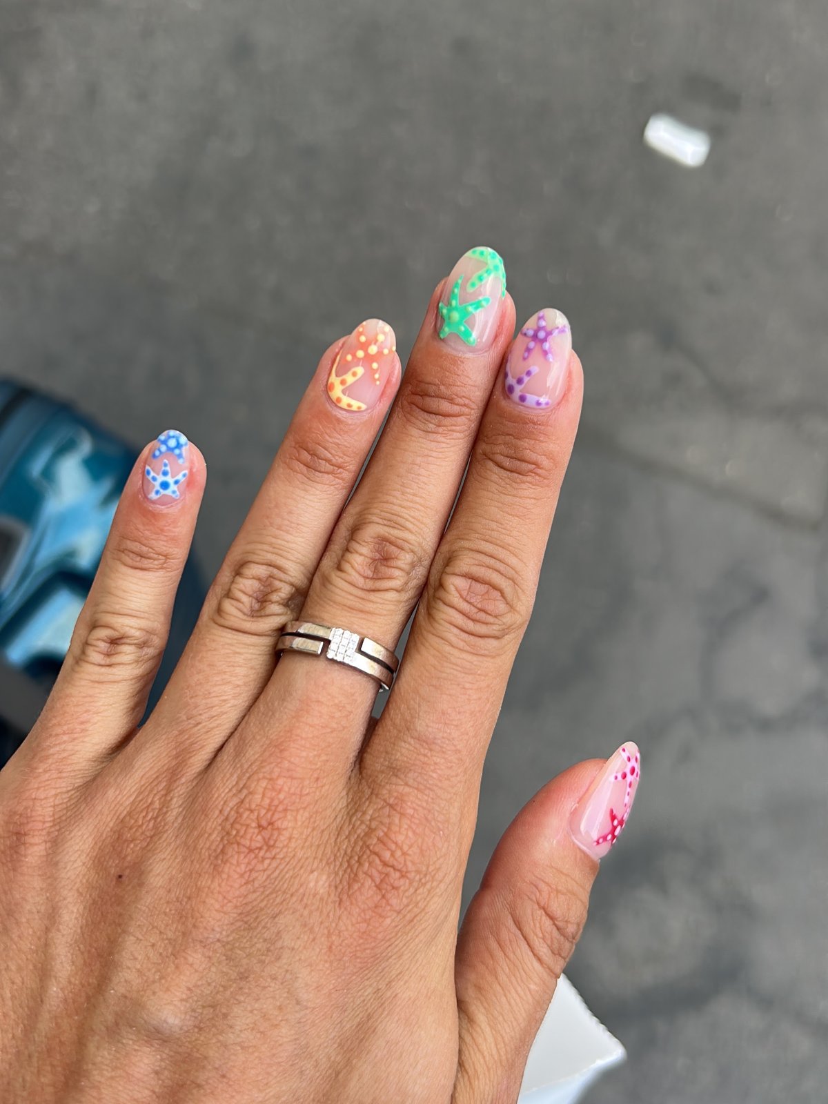 Nail art étoiles de mer à pois, une couleur par ongle (bleu, orange, vert, violet, rose) sur base nude, ongles amande — You Rêve Paris