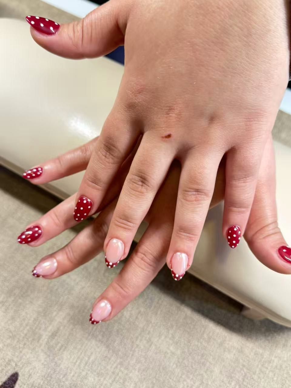 Mains croisées, ongles en amande rouges à pois blancs et french rouge à pois sur base rose nacrée